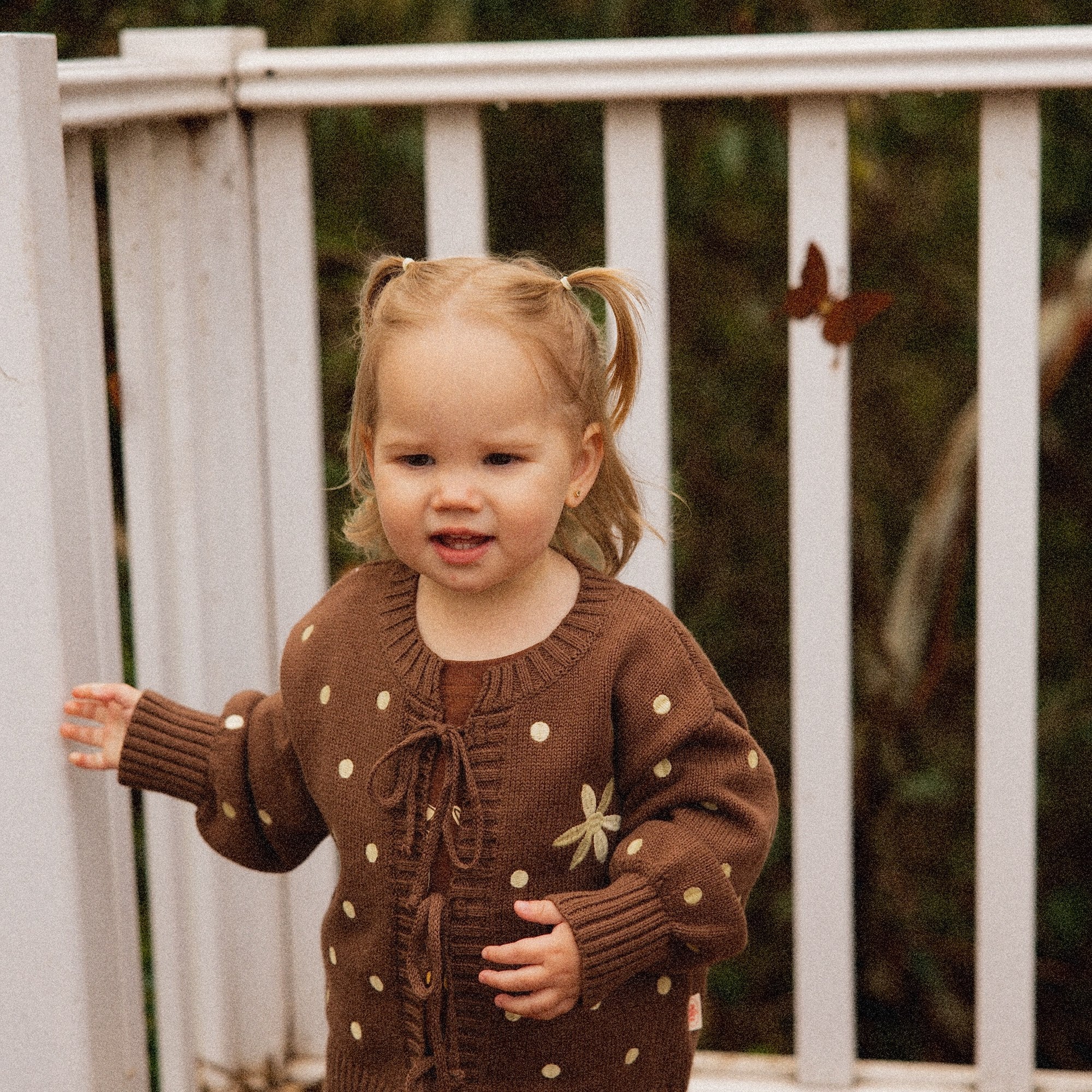 Toddler on a deck in the Honey Blossom Cardi, showing the tie front and buttery dot detail