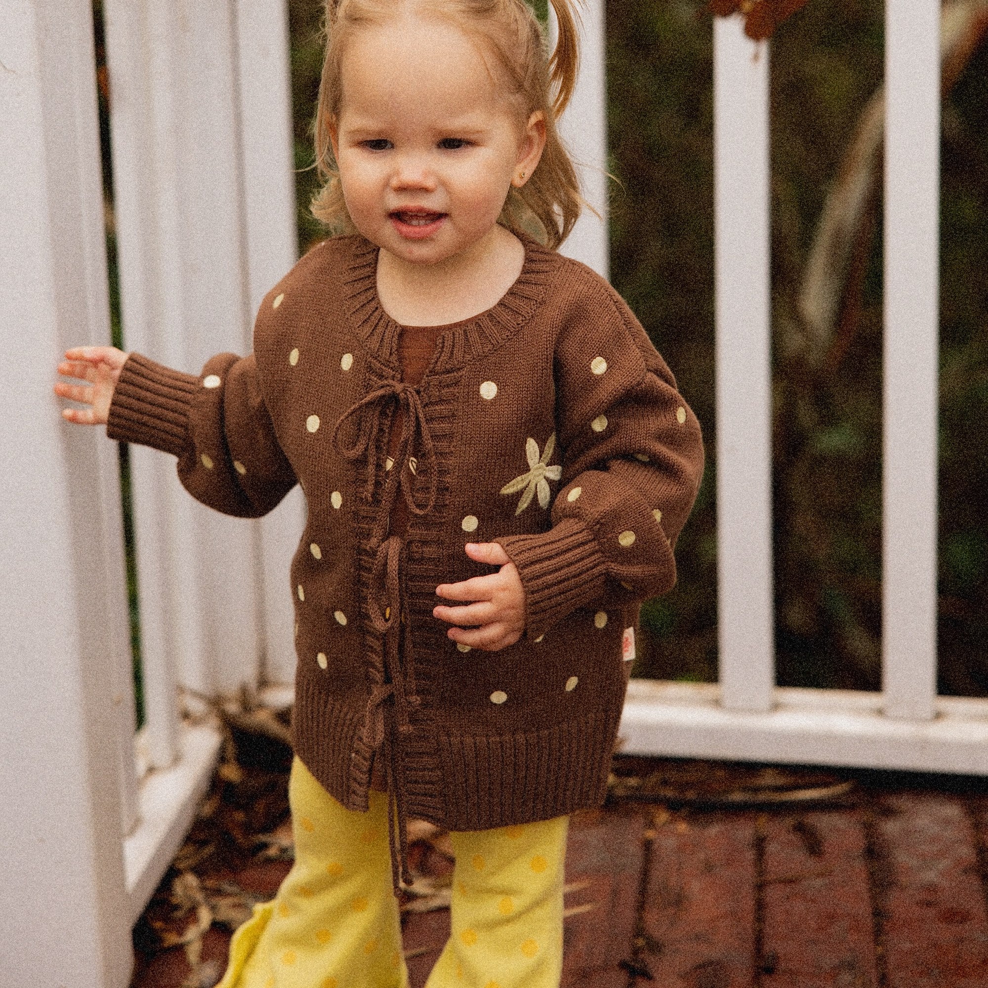 Toddler on a deck in the Buttercup Flares and Honey Blossom Cardi