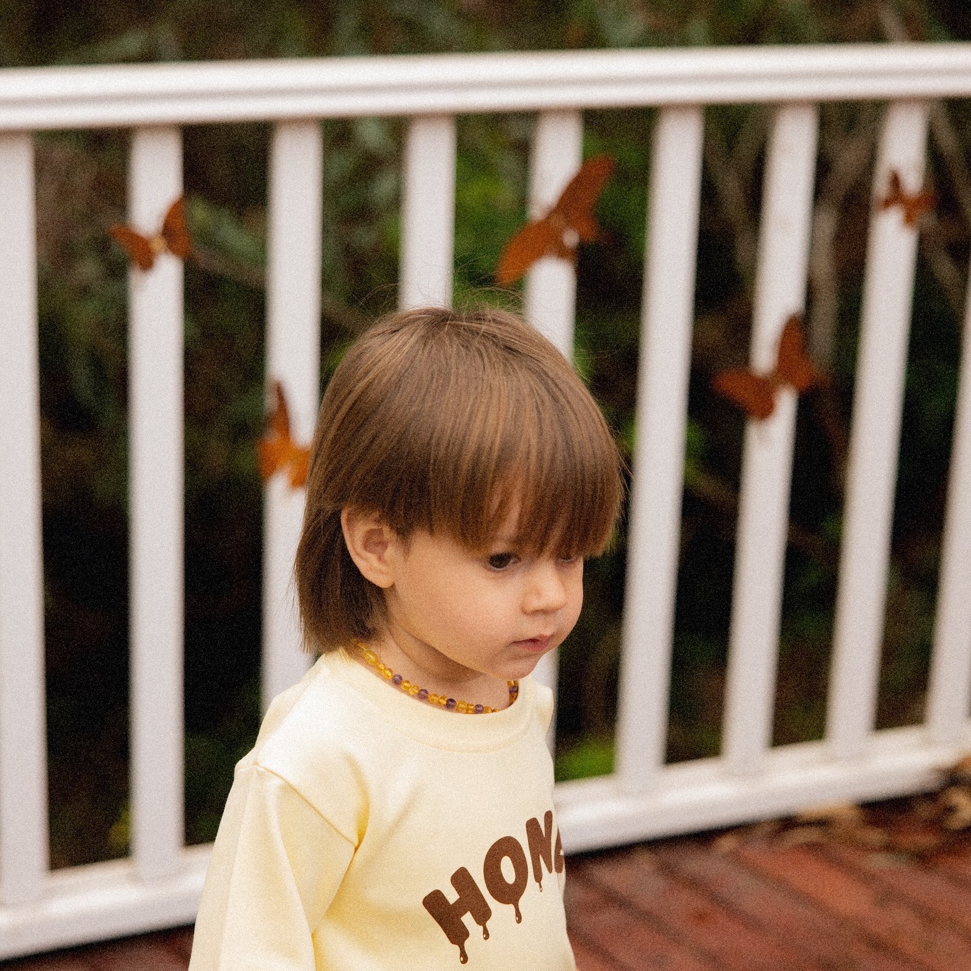 Child on a deck in the Sweet as Honey Tee, showing the dripping honey lettering
