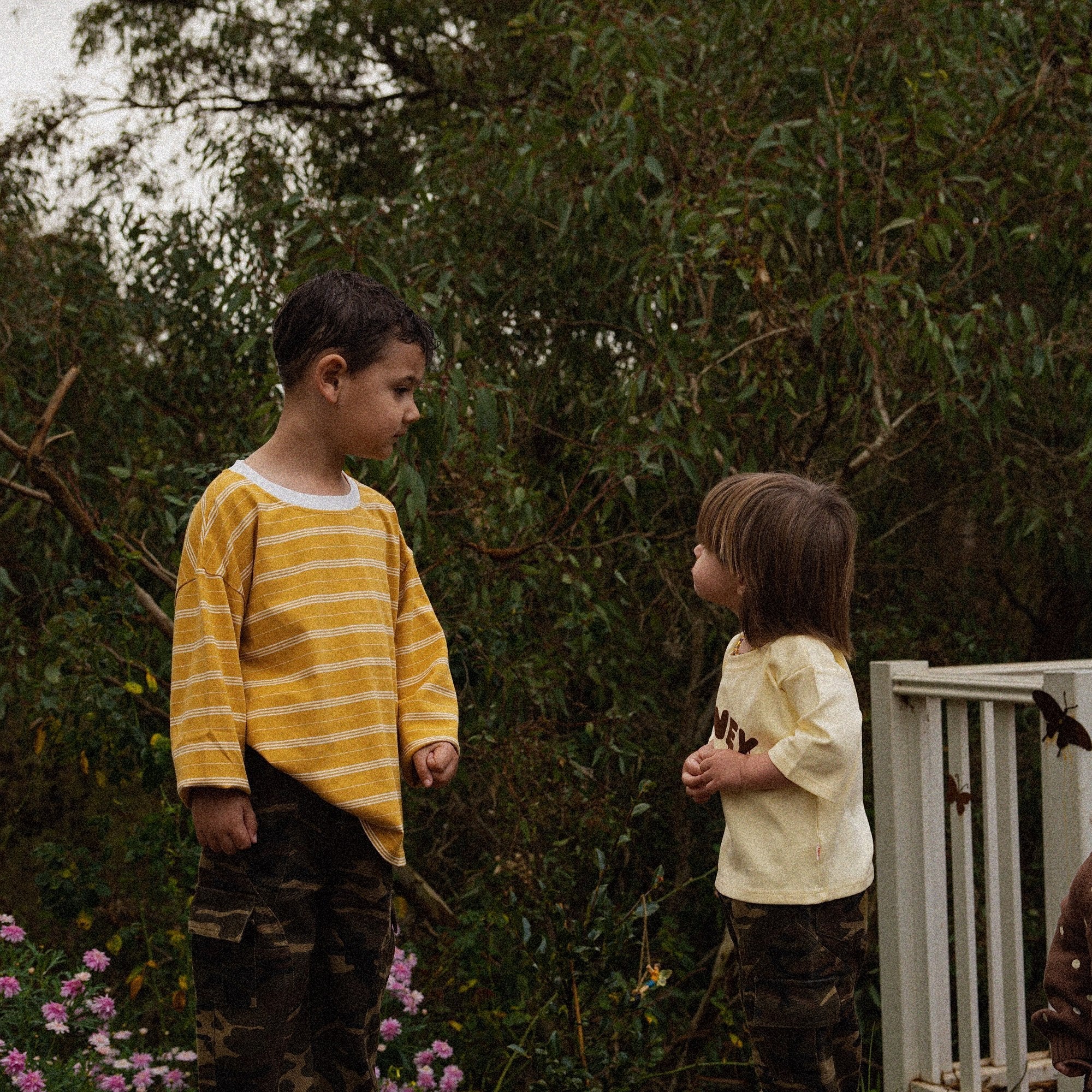 Two children on tree stumps, one in the Last Light Long Sleeve and Garden Explorer Cargos