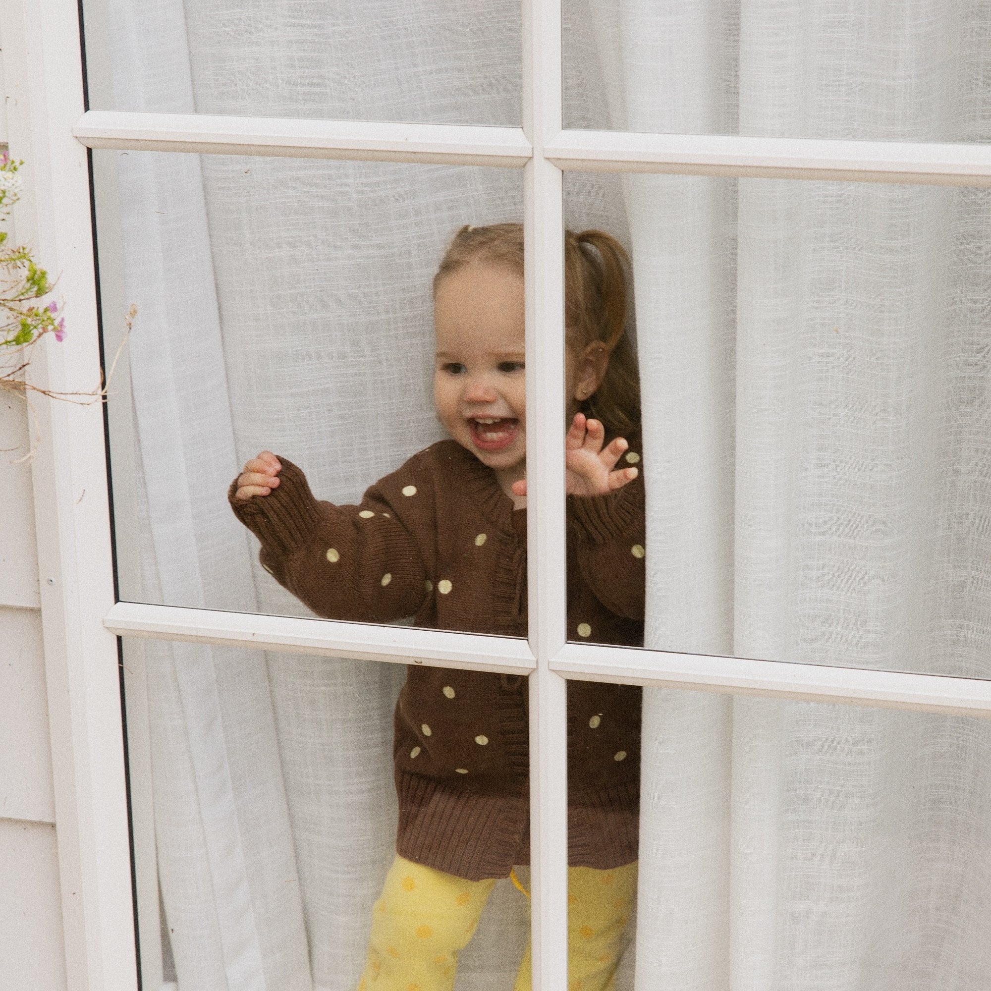Toddler laughing at a window in the Honey Blossom Cardi