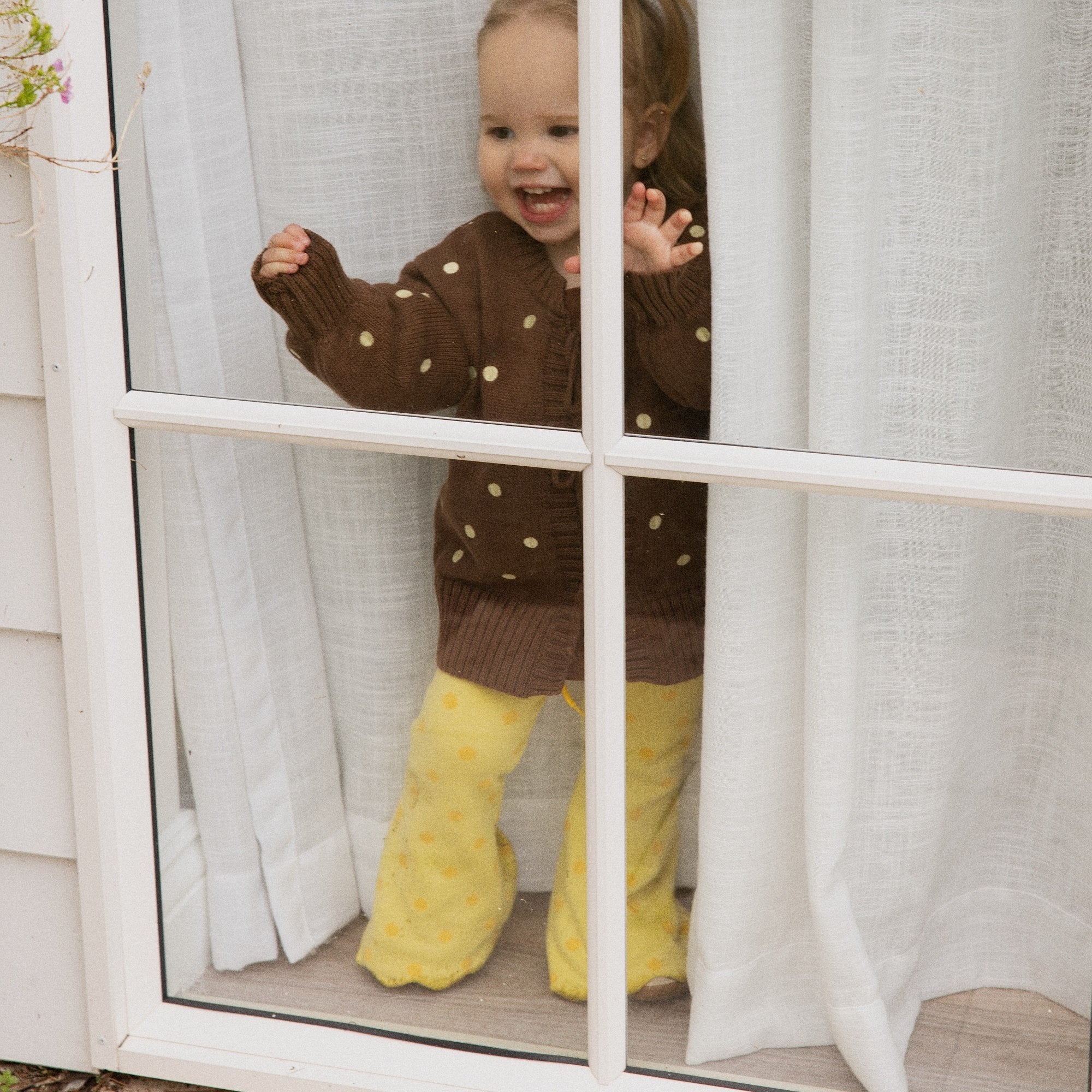 Toddler at a window in the Buttercup Flares in buttery yellow knit with gold spots