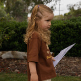Child in the garden wearing the Golden Hour Garden Tee, showing the hand drawn flower and bee print