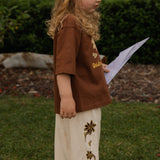 Child in the Let's Pick Flowers Pants in cream linen, embroidered flowers down the leg