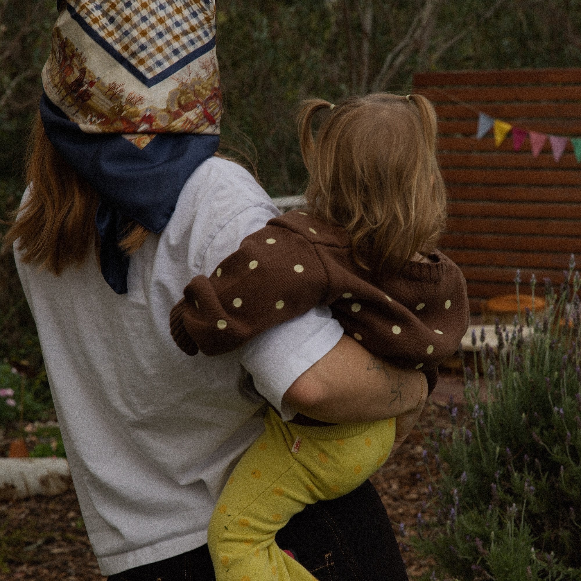 Mother carrying a toddler wearing the Honey Blossom Cardi in the garden