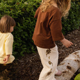 Two children in the garden, one wearing the Let's Pick Flowers Pants