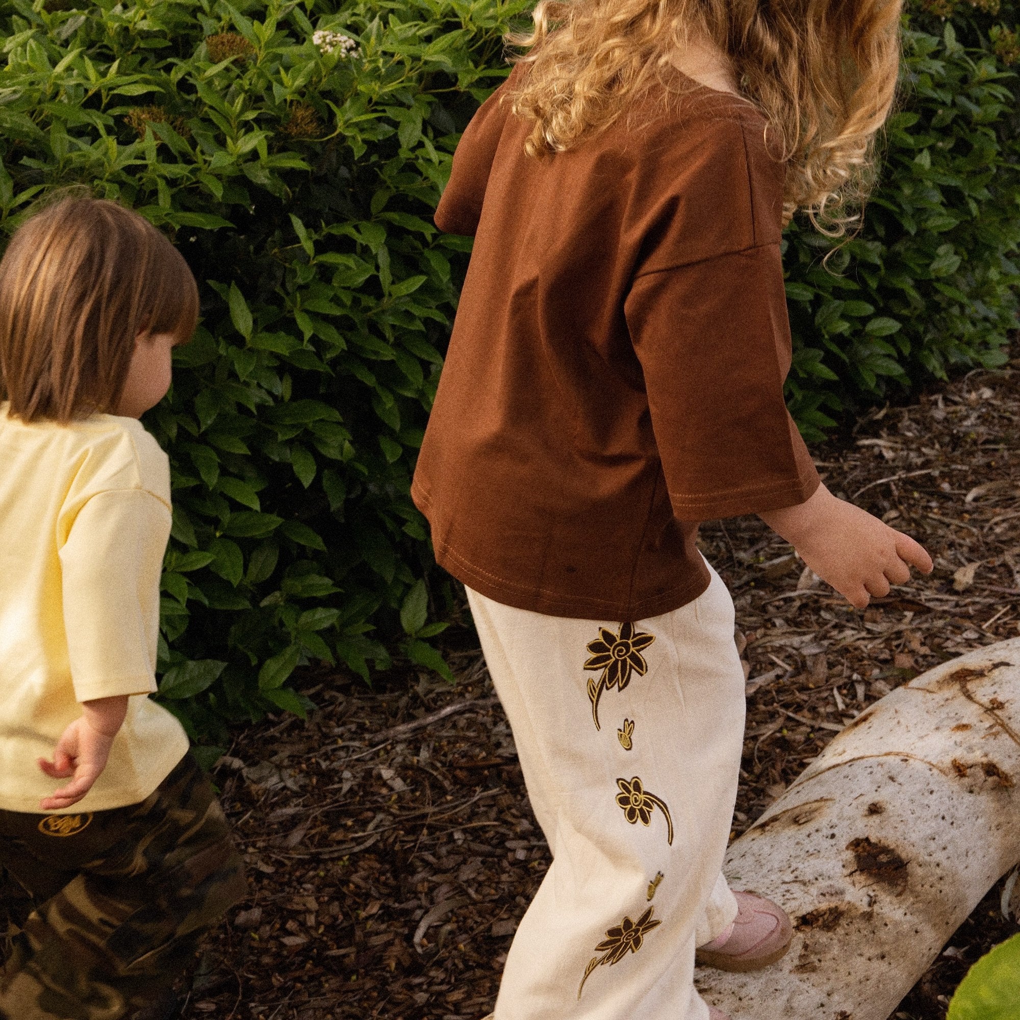 Two children in the garden, one wearing the Let's Pick Flowers Pants