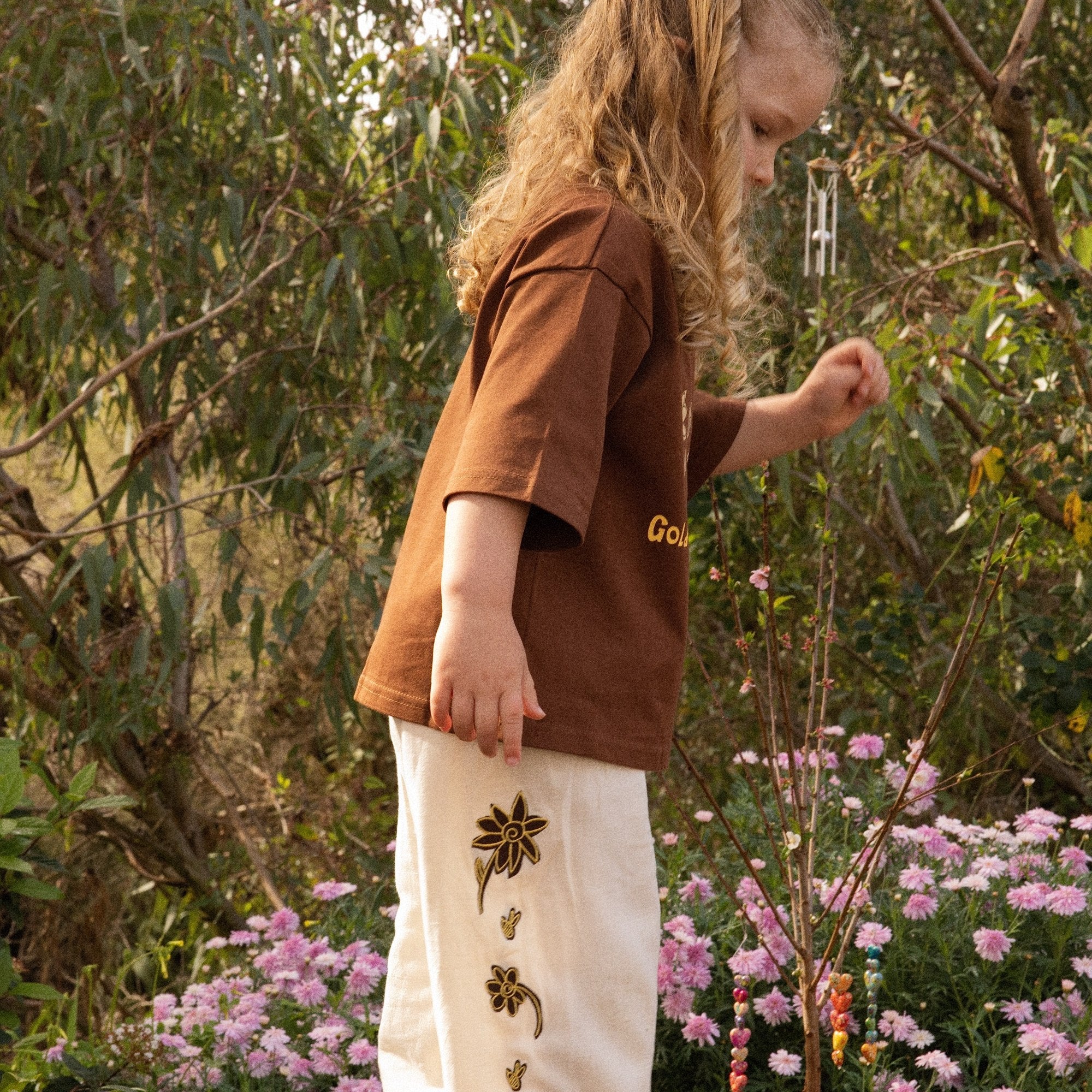 Child standing on a tree stump in the Golden Hour Garden Tee and Let's Pick Flowers Pants