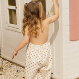 Child ringing a bell at a cubby house in the Daisy Dot Jumpsuit, showing the scoop back and wide leg