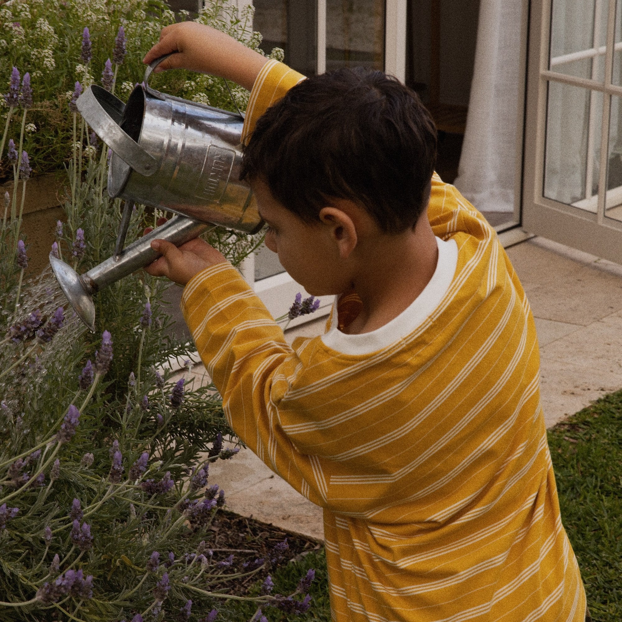 Child watering lavender in the Last Light Long Sleeve and Garden Explorer Cargos