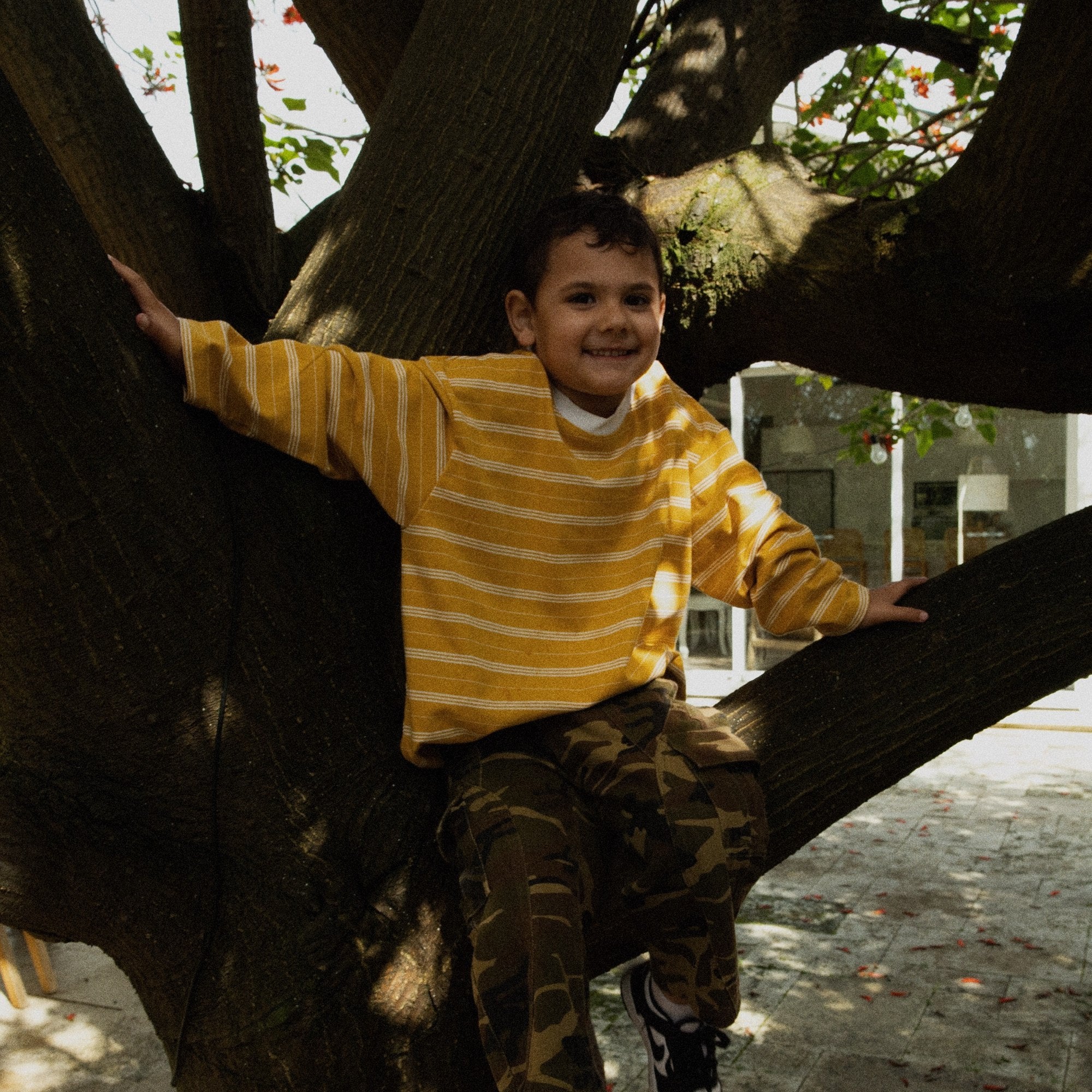 Child sitting in a tree in the Last Light Long Sleeve and Garden Explorer Cargos
