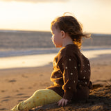 Toddler sitting on the sand at sunset in the Honey Blossom Cardi and Buttercup Flares