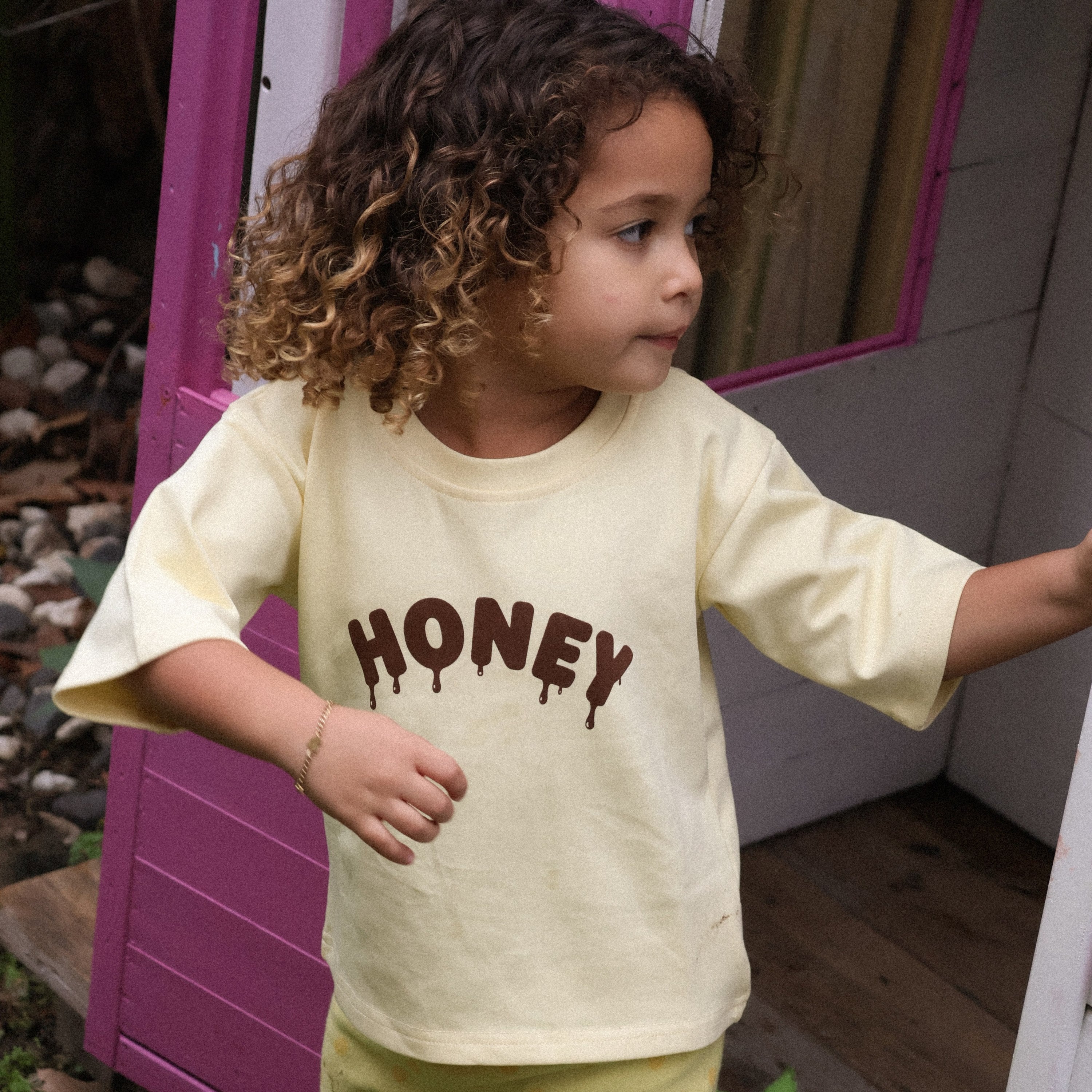 Child stepping out of a cubby house in the Sweet as Honey Tee and Buttercup Flares