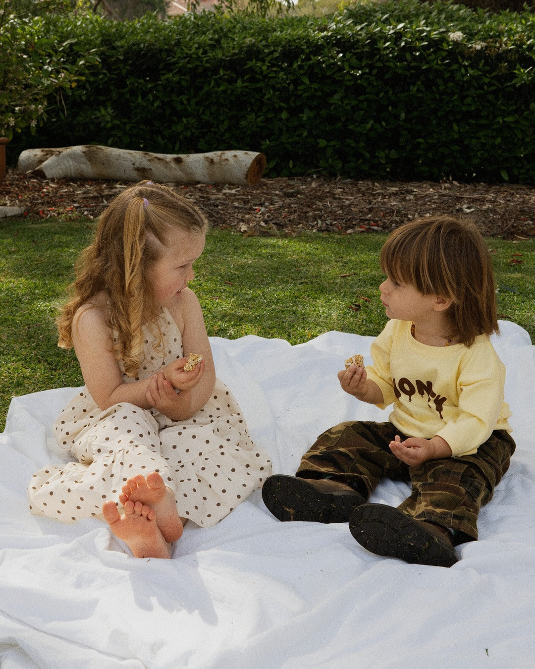 Two children on a picnic rug in the Sweet as Honey Tee and Garden Explorer Cargos