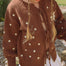 Child wearing the Honey Blossom Cardi in chocolate brown knit with cream polka dots, tie-up front and flower detail on the sleeve, paired with a white skirt